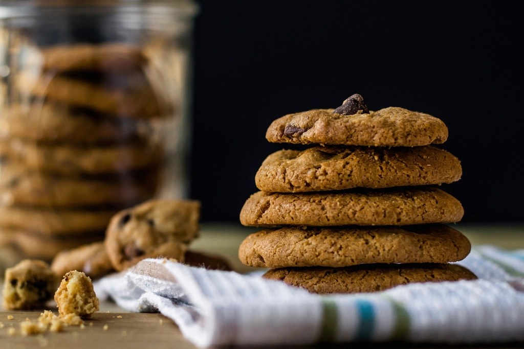 A stack of chocolate chip cookies beside a jar of cookies