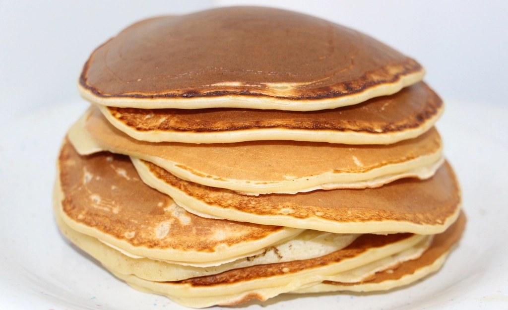 A tall stack of golden buttermilk pancakes on a white plate