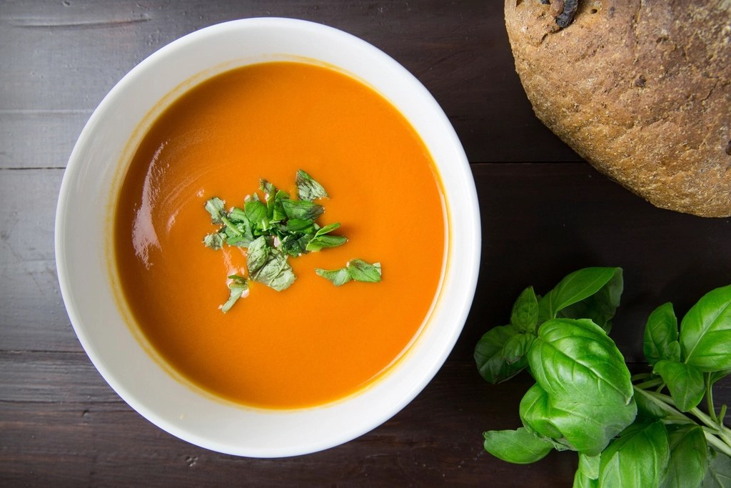 A bowl of tomato soup with fresh basil and crusty bread